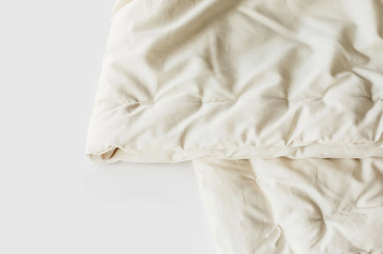 Stitched with care, you get warmth, temperature regulation, and breathability in this signature handmade product. Designed and handcrafted for comfort and coziness, our quilted comforters are made from domestically sourced premium eco wool encased in an organic cotton sateen shell. Hand-tufted and stitched around the perimeter so the wool batting stays in place. Now with corner ties for securing into your duvet cover. These comforters naturally regulate body temperature while wicking away moisture, ensuring