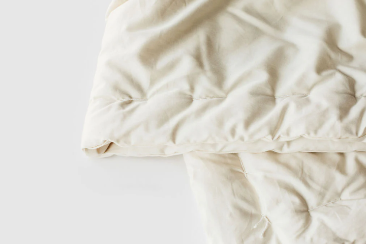 Designed and handcrafted for comfort, warmth and coziness, our certified organic quilted comforters are made from GOTS-certified wool encased in GOTS-certified organic cotton sateen. Hand-tufted and stitched around the perimeter so the wool batting stays in place. Now with corner ties for securing into your duvet cover. These comforters naturally regulate body temperature, ensuring a restful sleep in any season. We offer three basic weights